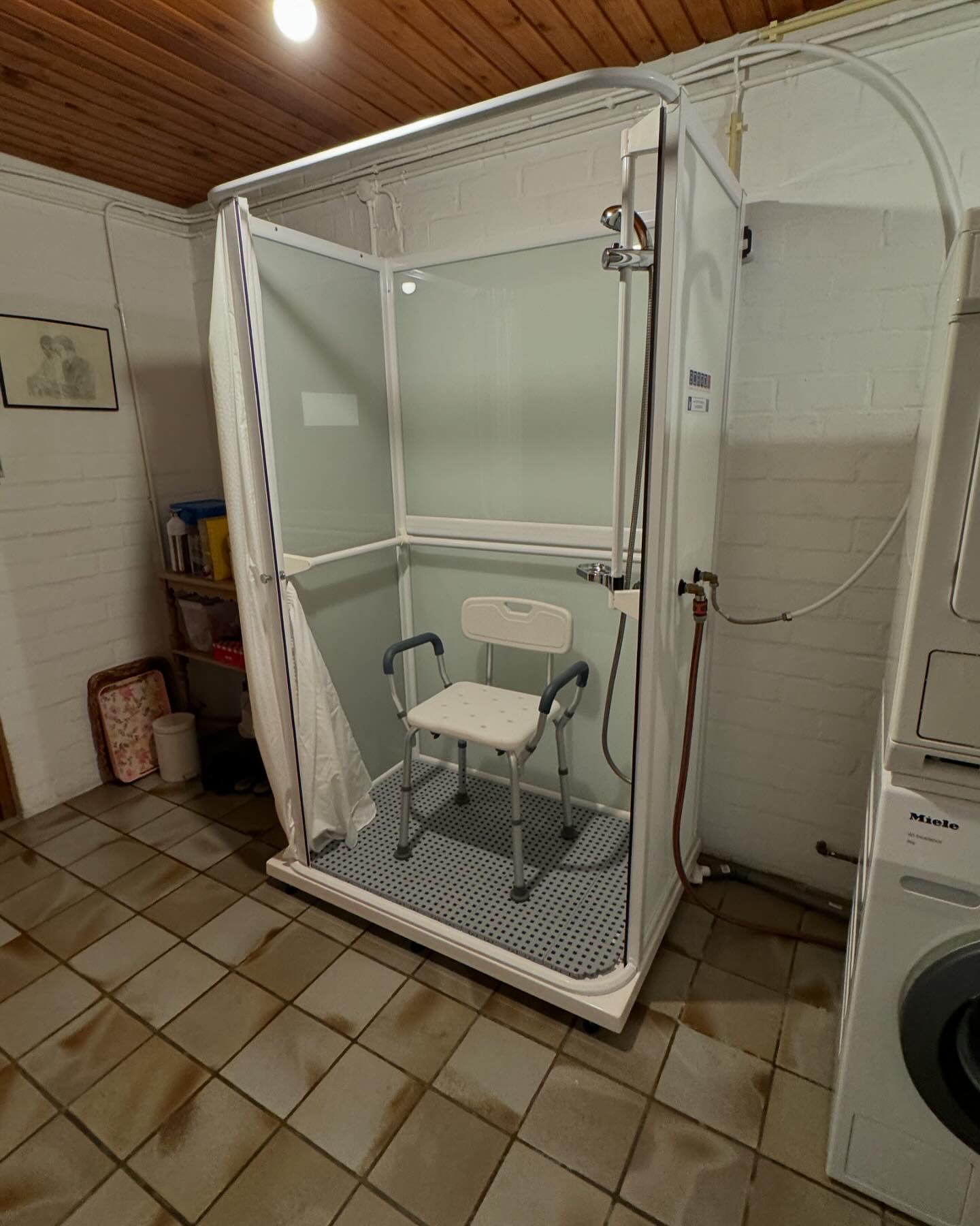 Mobiele zorgdouche van Borro-Rental met geopende cabine en douchestoel, geplaatst in een wasruimte thuis