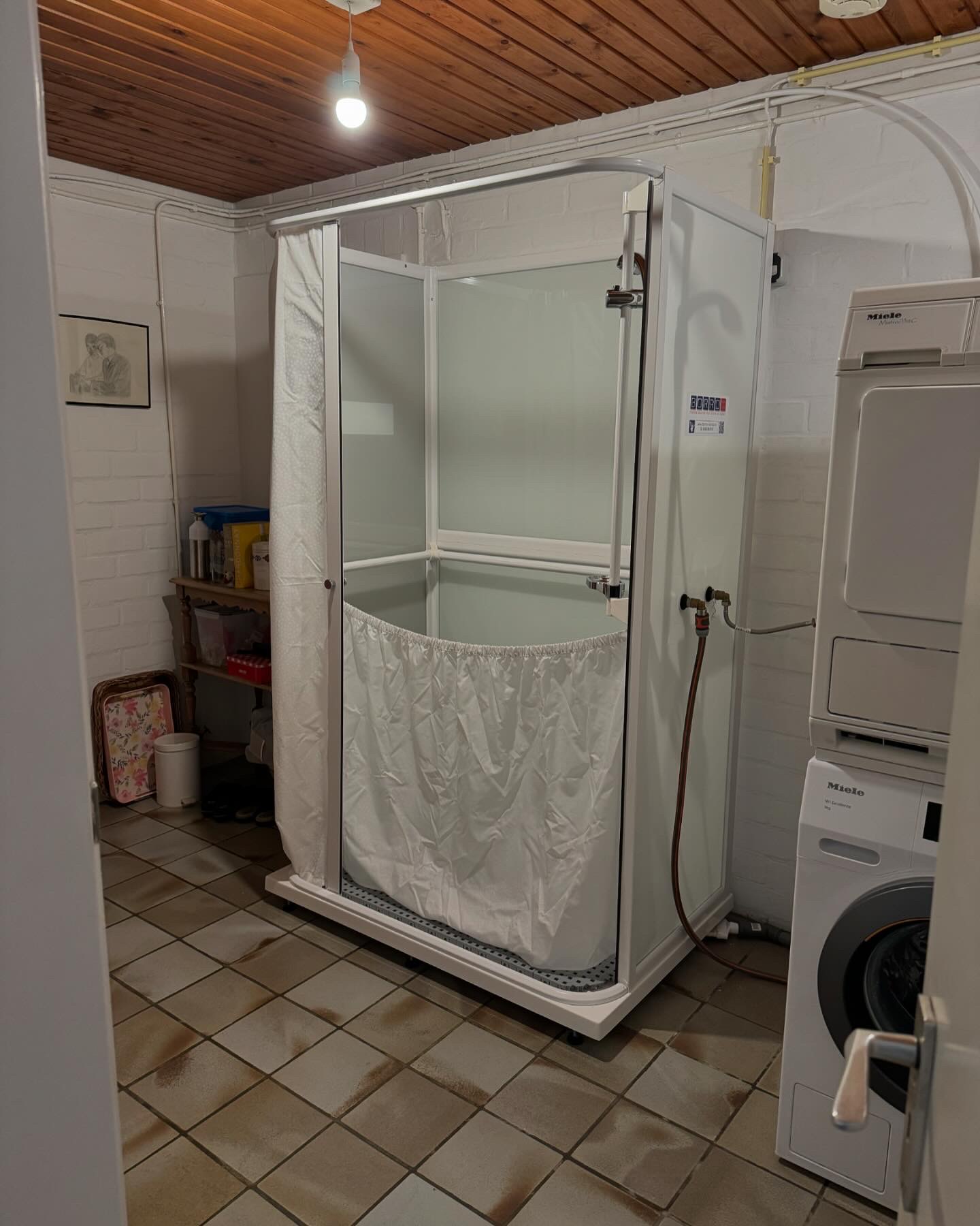 Mobiele zorgdouche geplaatst in een ruime bijkeuken/wasruimte, aangesloten op de bestaande warm- en koudwatervoorziening.