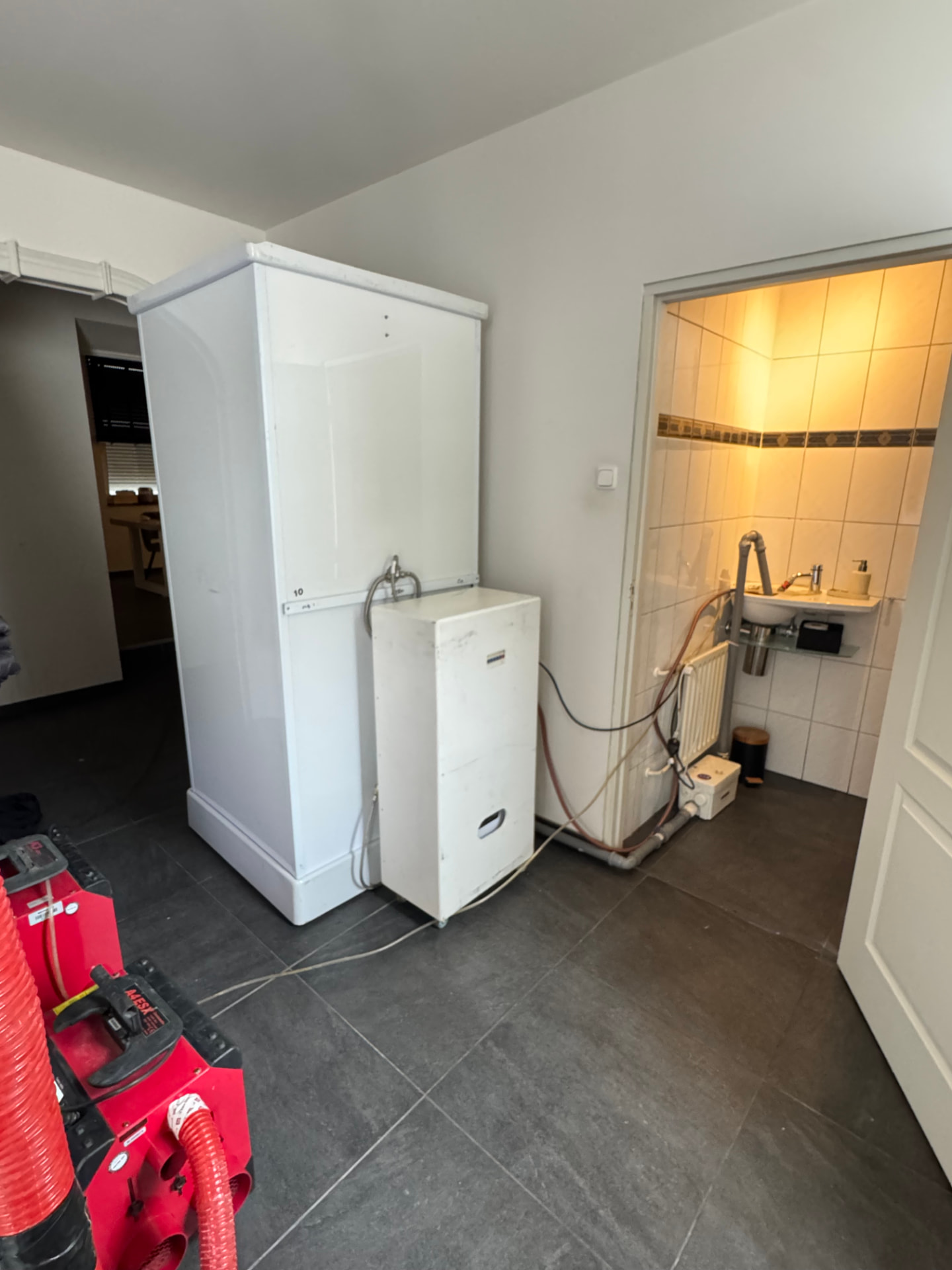 Mobiele douchecabine met boiler en vuilwaterpomp in de gang van een woning in Kerkrade-Centrum